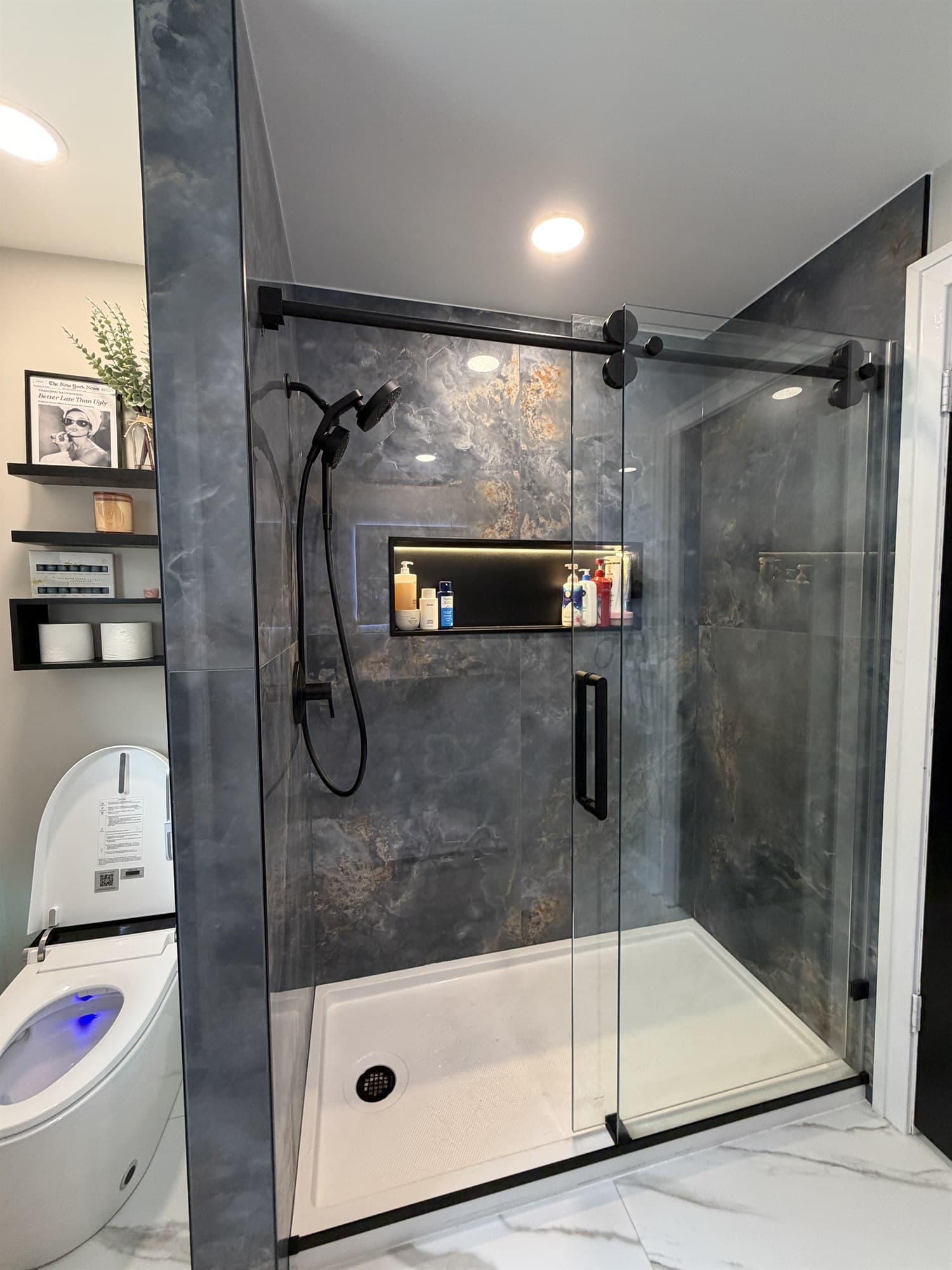 Walk-in shower finished in dark slate-look porcelain tile with a black sliding glass door and a lit recessed niche