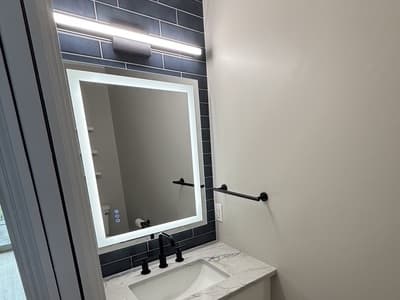 Half bath with navy subway tile, backlit mirror, black fixtures and white vanity