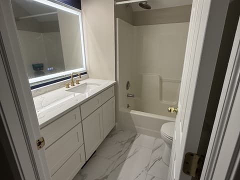 Bathroom with marble-look flooring, white vanity, gold faucet and tub-shower combo