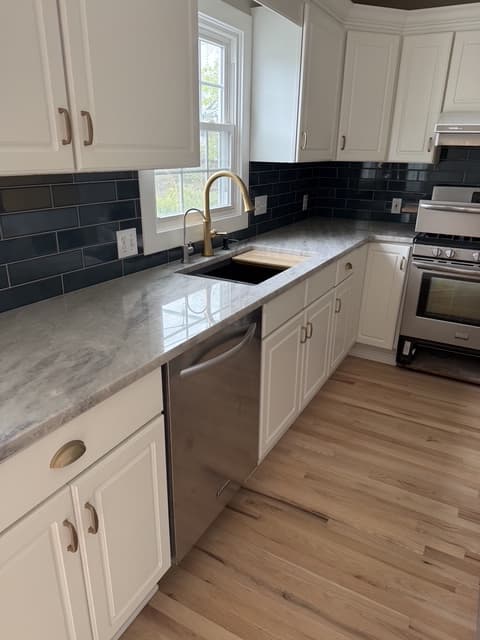 White shaker kitchen with navy tile backsplash, gold faucet and marble-look counters